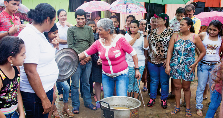 A hot meal: Urrego (beneath the green umbrella) and her neighbours enjoy a shared pot of stew.