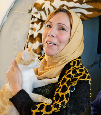 Foto der 47-Jährigen Nada Yussuf Kada vom seitlichen Profil mit Blick in die Kamera. Sie lächelt, trägt ein gelbes Kopftuch und ein Oberteil mit Leopardenmuster. In der Hand hält sie eine weiß-orange Katze.