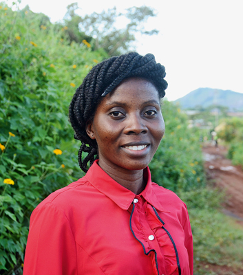 Porträt der Agrarwissenschaftlerin und „Farmer Business School“-Trainerin Fadeke Omolabake Adeoye in Nigeria. Sie lächelt, trägt eine rote Bluse und steht vor einer grünen Hecke.