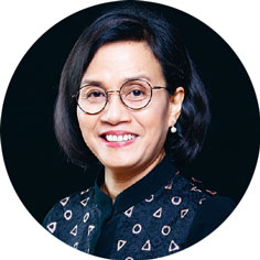 Porträt von Sri Mulyani Indrawati, eine indonesische Ökonomin. Sie trägt eine Brille mit rundem Gestell und ein dunkles, gemustertes Oberteil. Ihr Haar ist kurz, stilvoll geschnitten und sie lächelt.