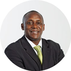 Portät von Kandeh Yumkella. Der mittelalte Mann trägt einen schwarzen Anzug, ein weißes Hemd und eine hellgrüne Krawatte. Seine Arme sind verschränkt und er blickt direkt in die Kamera. Der Hintergrund ist einheitlich hell und schlicht.