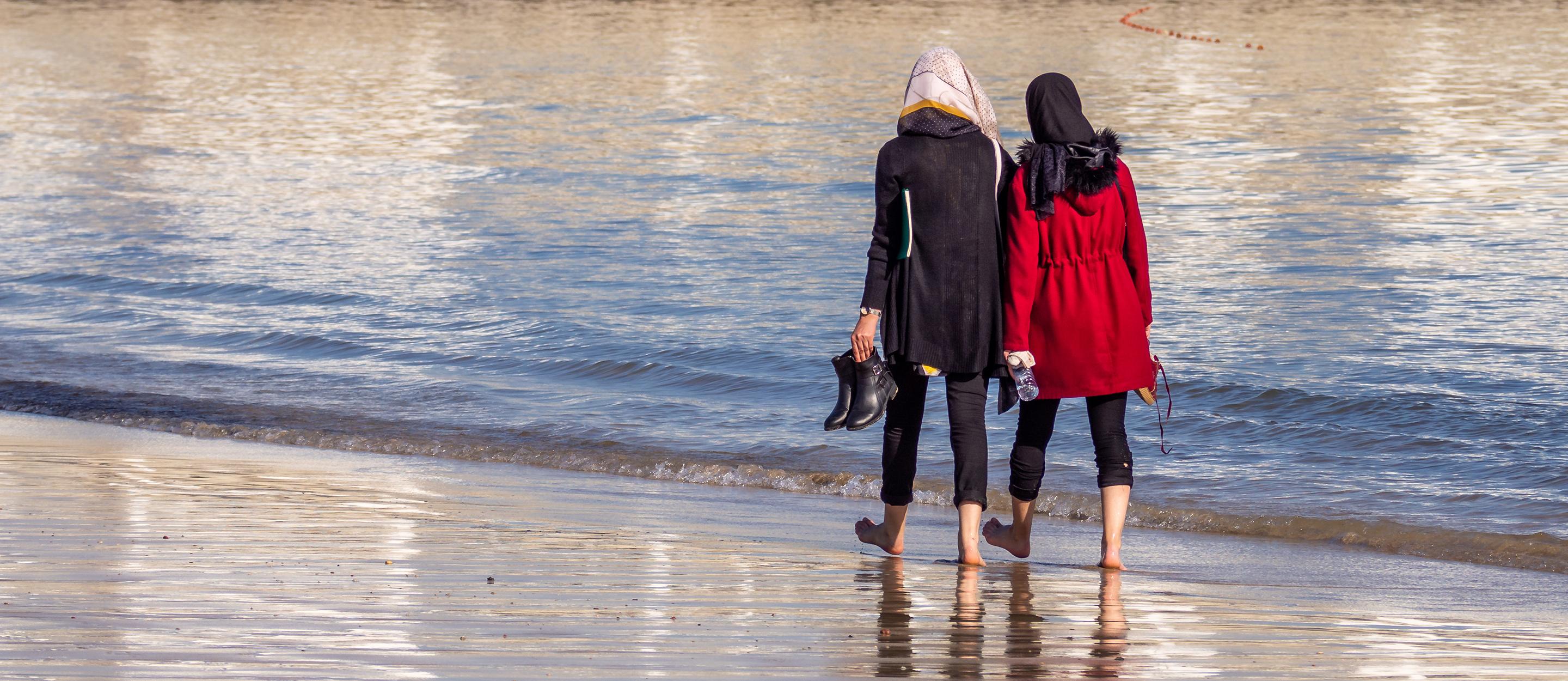 Zwei Frauen laufen am Strand mit dem Rücken zum Betrachter