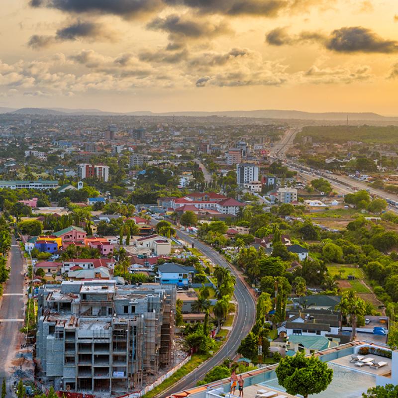 Aufnahme aus der Luft auf eine afrikanische Großstadt bei Sonnenuntergang, mit dichter Bebauung, Straßen, umgeben von üppigem Grün.