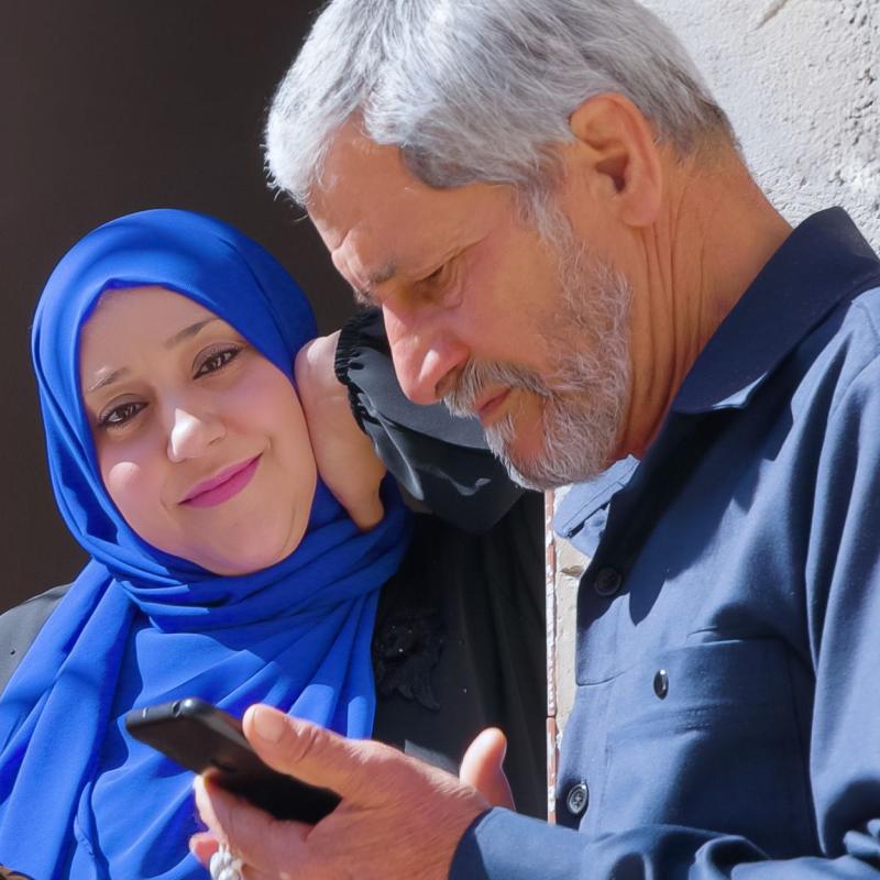 Zwei Frauen mit Kopftuch und ein Mann am Handy