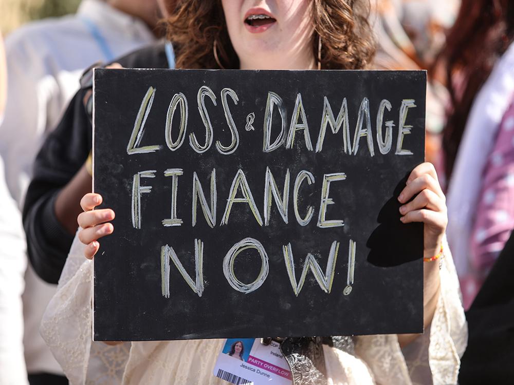 Woman with sign "LOSS & DAMAGE FINANCE NOW!"