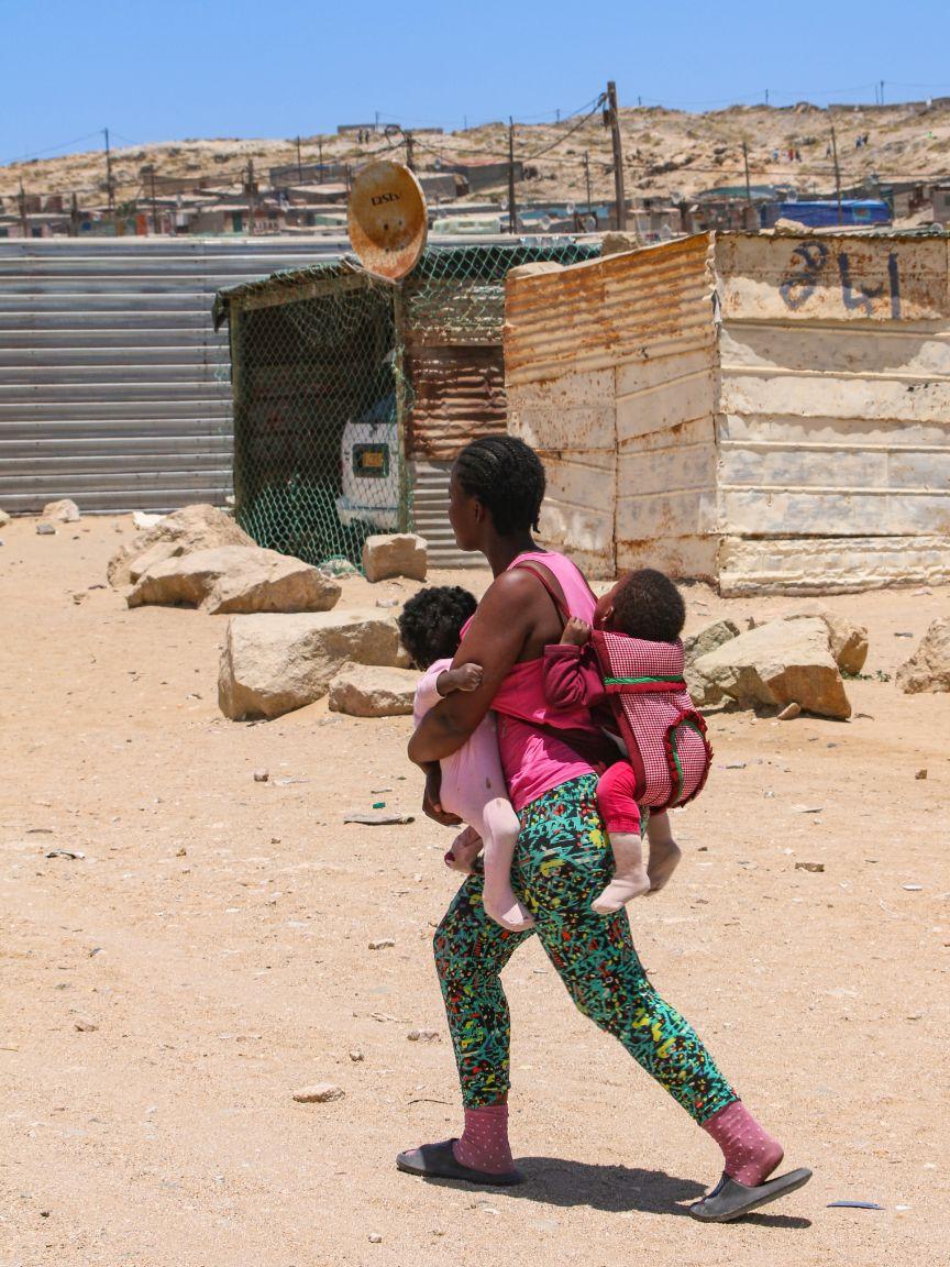 Frau trägt zwei Kinder in einer Trage