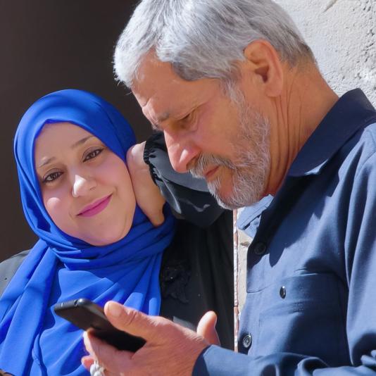 Zwei Frauen mit Kopftuch und ein Mann am Handy